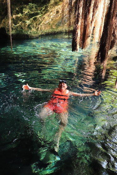 A person floating in clear water with moss-covered rocks and hanging roots. 3