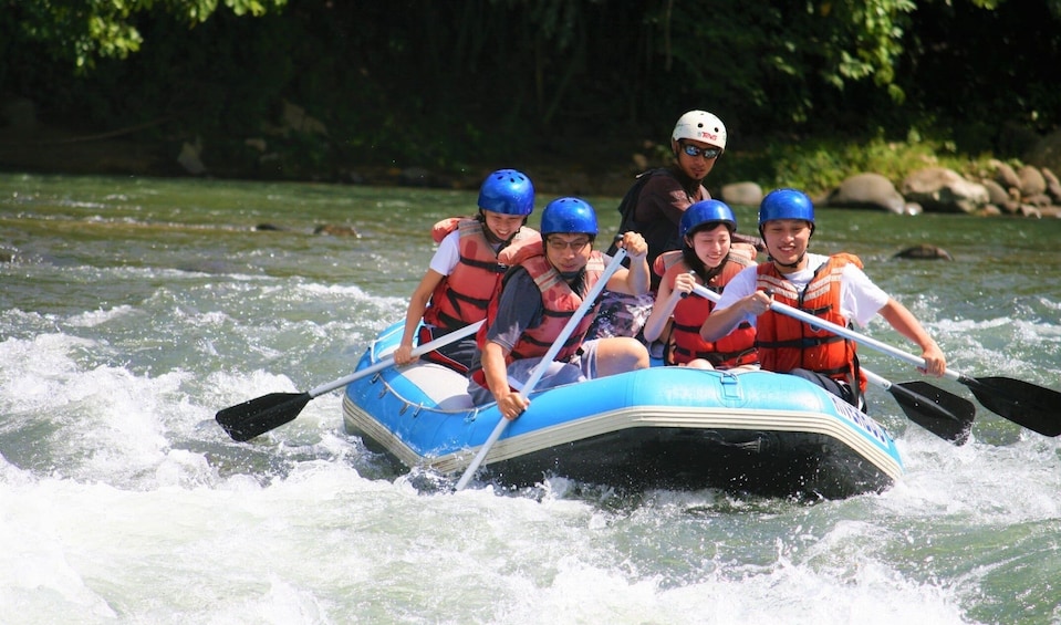 Een groep mensen in een blauwe luchtbed op een rivier, met reddingsvesten en helmen. 2