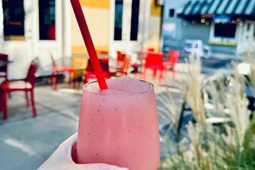 A pink drink with a red straw in a glass, held by a hand. 1