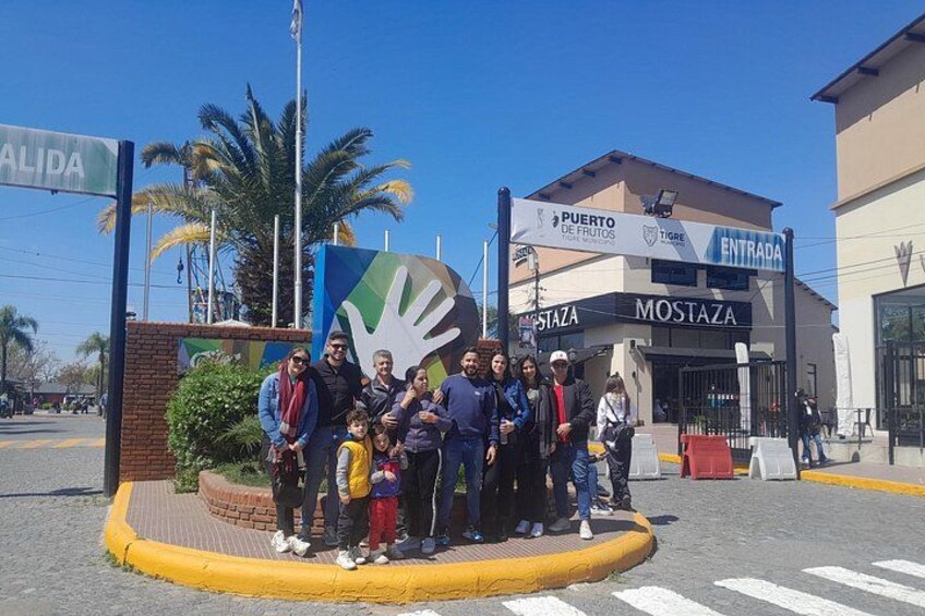 Un groupe de personnes se tient devant un bâtiment orné d’un logo représentant une empreinte de main et de panneaux indiquant « Puerto de Frutos » et « Mostaza ». 5