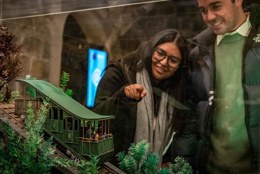 A model train set with a green locomotive and carriages, surrounded by miniature trees and a stone wall. 4