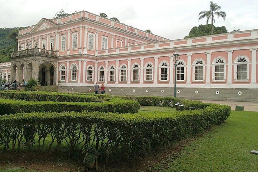 Ein großes, rosafarbenes und weißes Gebäude mit Rundbogenfenstern und einem formalen Garten davor. 1