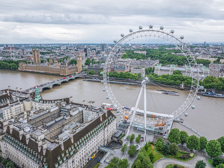 A cityscape with a prominent Ferris wheel, the River Thames, and historic buildings including the Houses of Parliament. 2