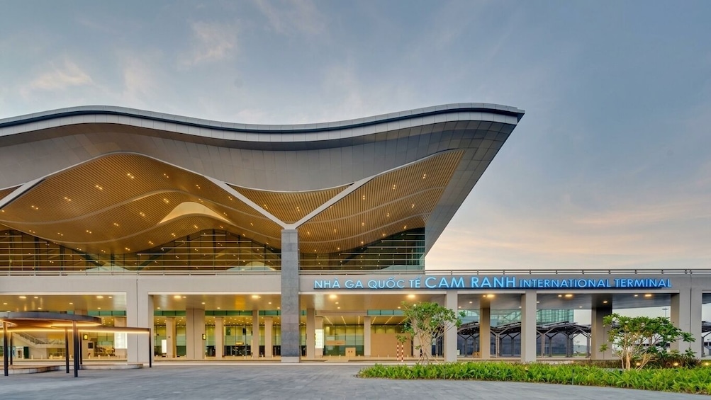 Un terminal d’aéroport au design moderne, doté d’un toit incurvé et d’une enseigne indiquant « TERMINAL INTERNATIONAL DE L’AÉROPORT DE CAM RANH ». 3