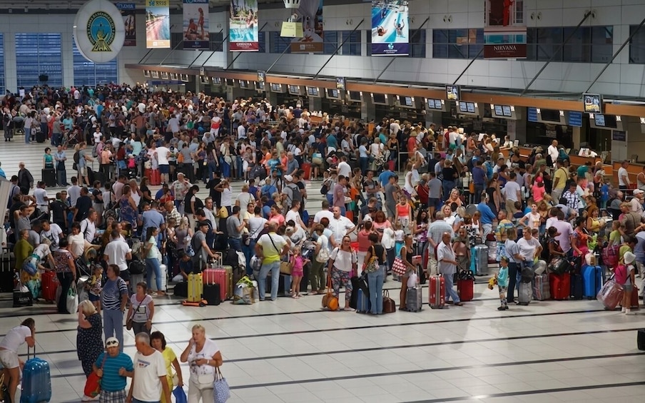 Un terminal d’aéroport bondé, où l’on voit des gens debout et en train de marcher, des bagages, ainsi que divers panneaux et publicités. 2