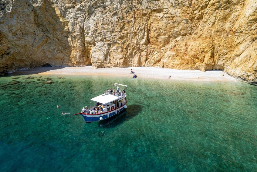 A boat with passengers in clear waters near a rocky cliff. 1