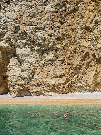 A rocky cliff and clear turquoise water with people swimming. 2