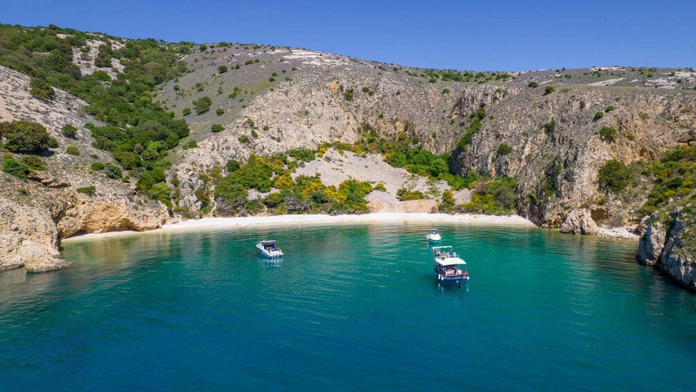A coastal landscape with clear turquoise waters, rocky cliffs, and boats anchored near the shore. 4