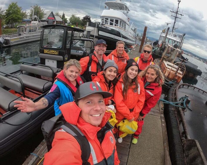 A group of people on a boat, wearing life jackets and orange jackets, with a boat named "BIG ANIMAL ENCOUNTERS" in the background. 5