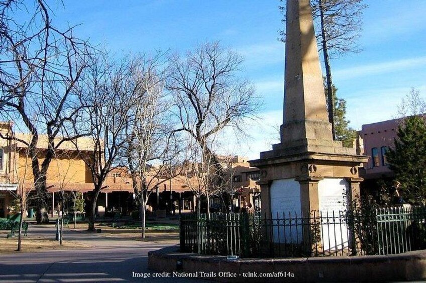A tall monument with a plaque, surrounded by bare trees and buildings. 2