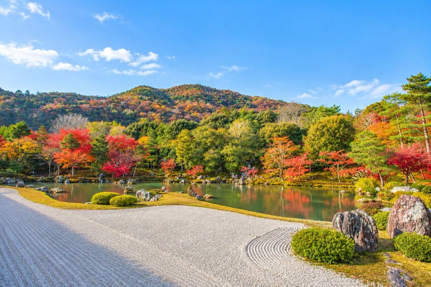 A serene Japanese garden with a pond, autumn foliage, and a mountainous backdrop. 4
