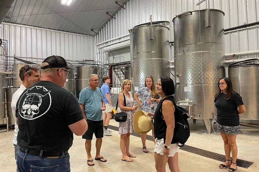 A group of people in a brewery with stainless steel tanks and a high ceiling. 3