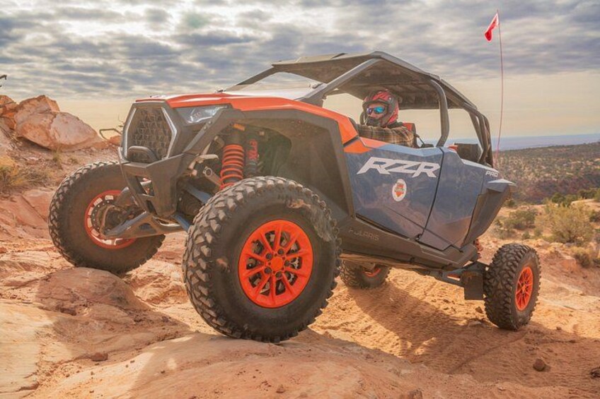 A RZR off-road vehicle on a rocky terrain with a flag on the windshield. 2
