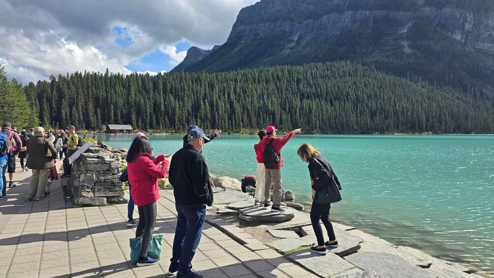 A group of people at a lakeside viewpoint with mountains in the background. 2