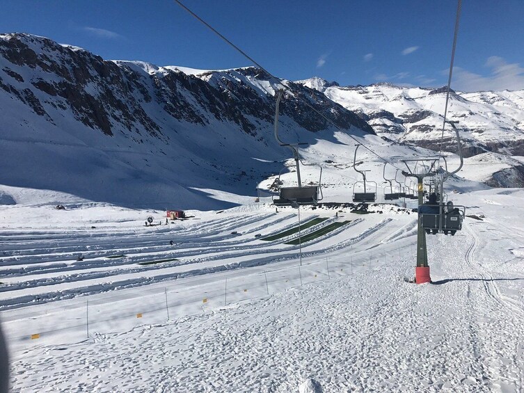 A ski lift with chairs moving up and down a snowy slope, surrounded by snow-covered mountains. 2