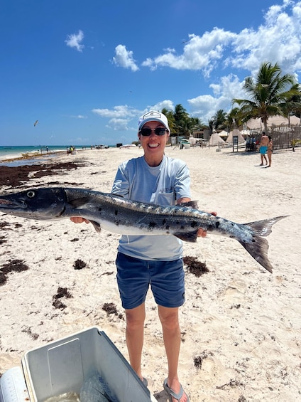A person holding a large fish on a sandy beach with palm trees and a clear sky in the background. 3