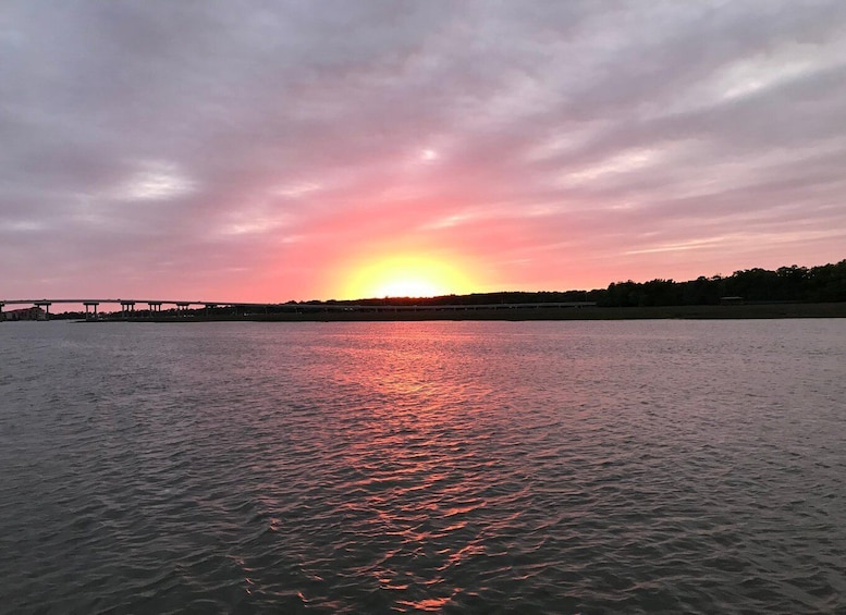 Solnedgang over et roligt vandareal med en bro i det fjerne. 5