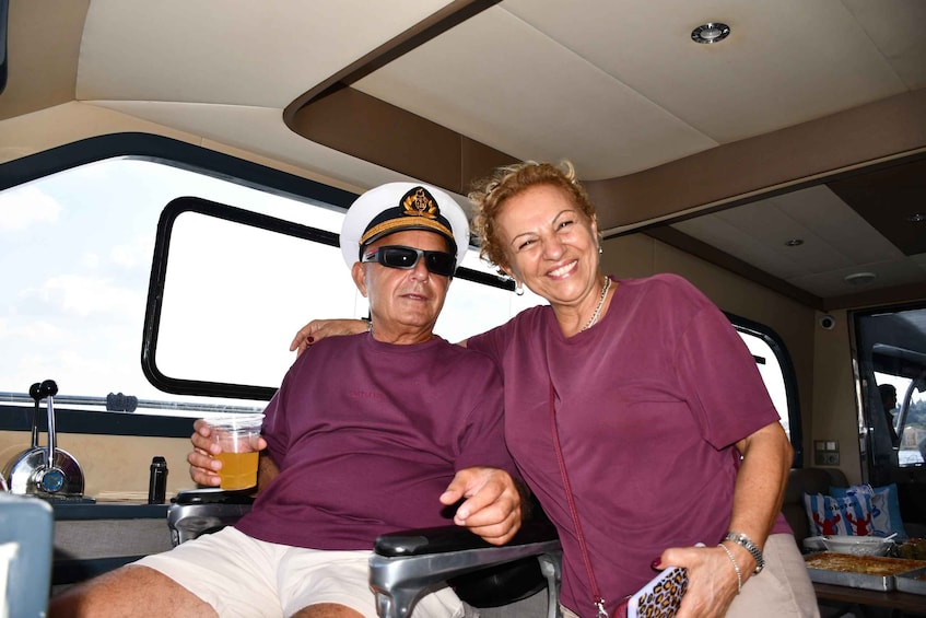A person in a purple shirt and a person in a white shirt with a captain's hat, both seated on a boat. 3