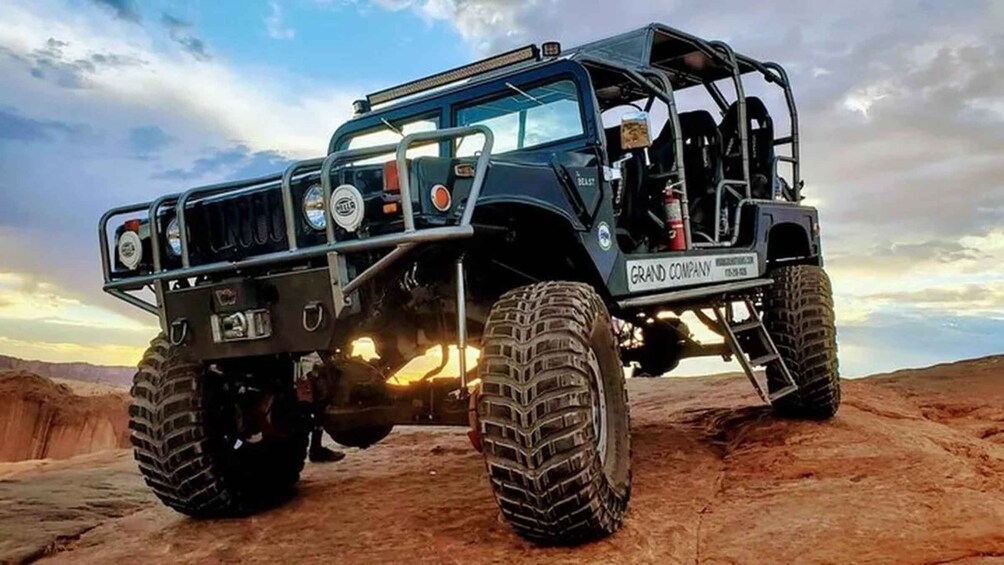 A rugged off-road vehicle with large tires and a raised suspension, parked on a rocky terrain under a cloudy sky. 1