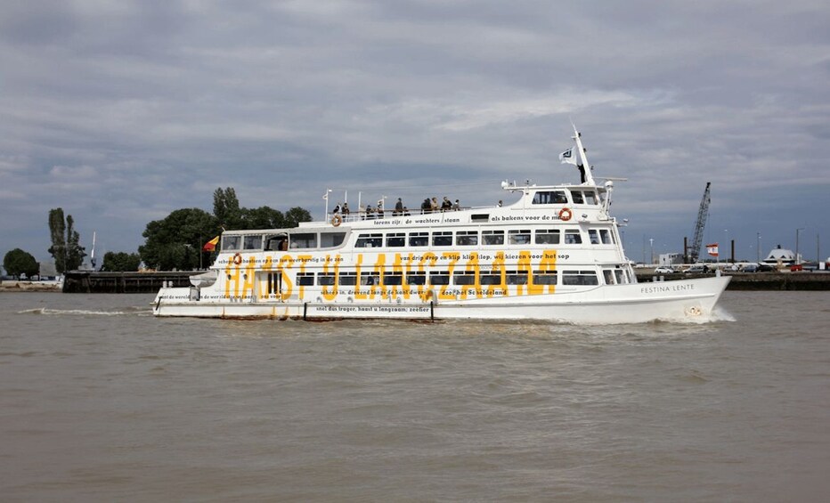 A white ferry with yellow text and a flag, moving on a river. 2