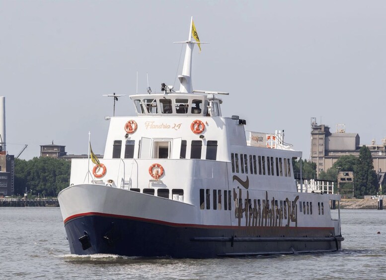 A ferry named 'Flandria 24' with lifebuoys and a yellow flag on its deck, sailing on a river with industrial buildings in the background. 5