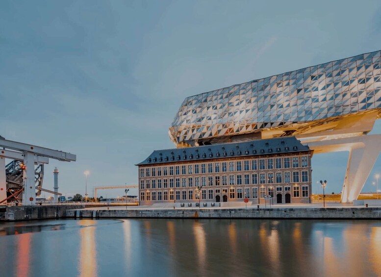 A modern building with a geometric facade and a large, white, curved structure above it, reflecting on a calm body of water. 3