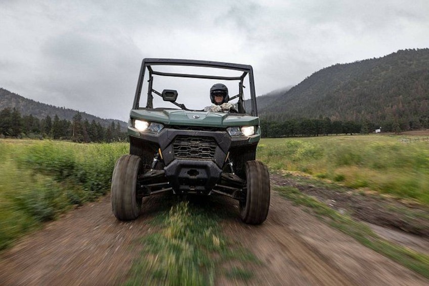 A green off-road vehicle driving on a dirt road with a forested mountain in the background. 3
