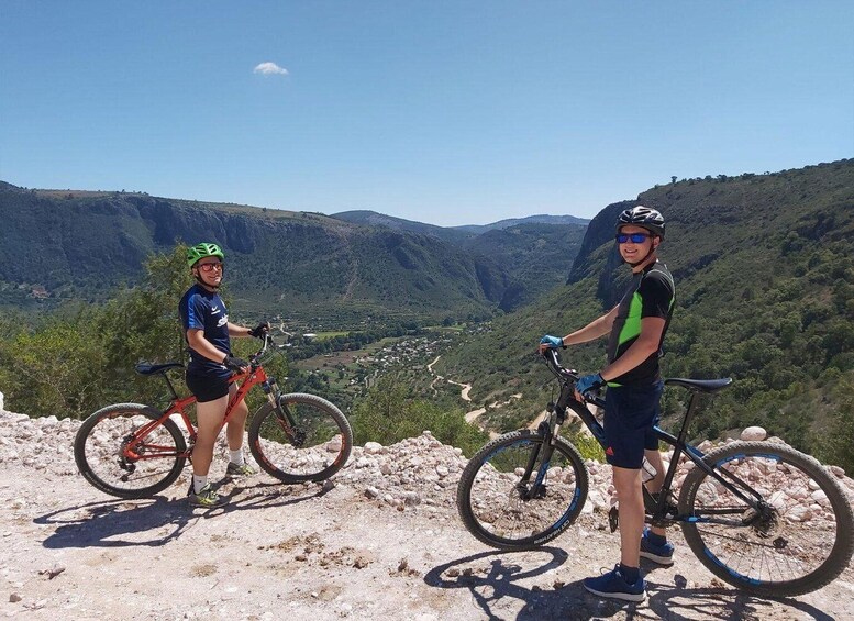 Two people on a mountain biking trail with a scenic view of a valley and hills in the background. 4