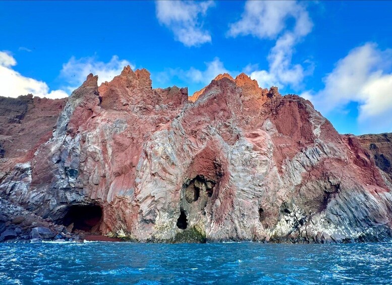 A rocky coastline with a prominent cave entrance and a clear blue sky. 3