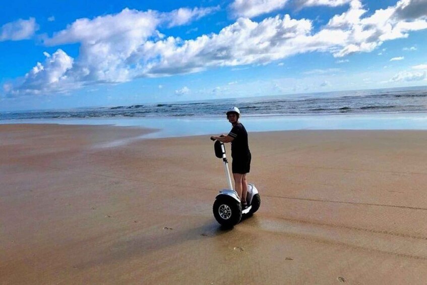 A person riding a hoverboard on a sandy beach with the ocean in the background. 1
