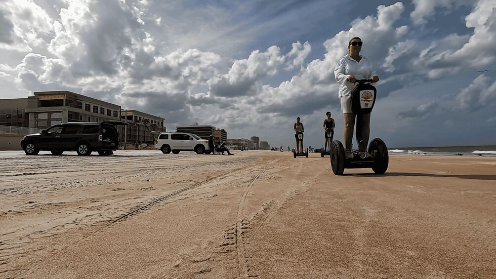 A beach with people riding Segways, a sandy path, and parked cars. 2