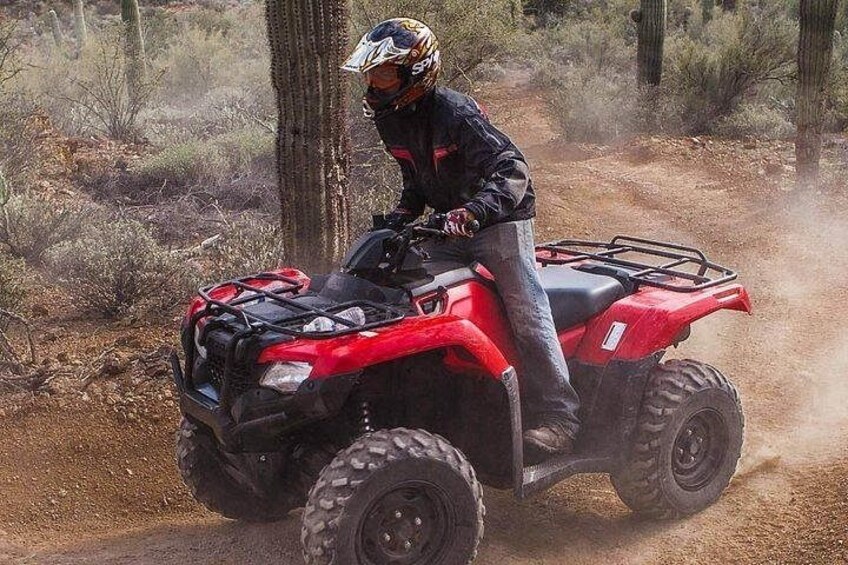 A person riding a red ATV on a dirt trail in a wooded area. 2