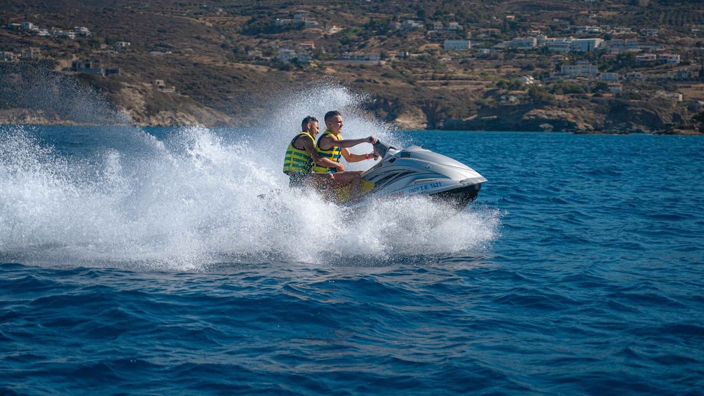 Two people jet-skiing on a lake with a coastal town in the background. 1