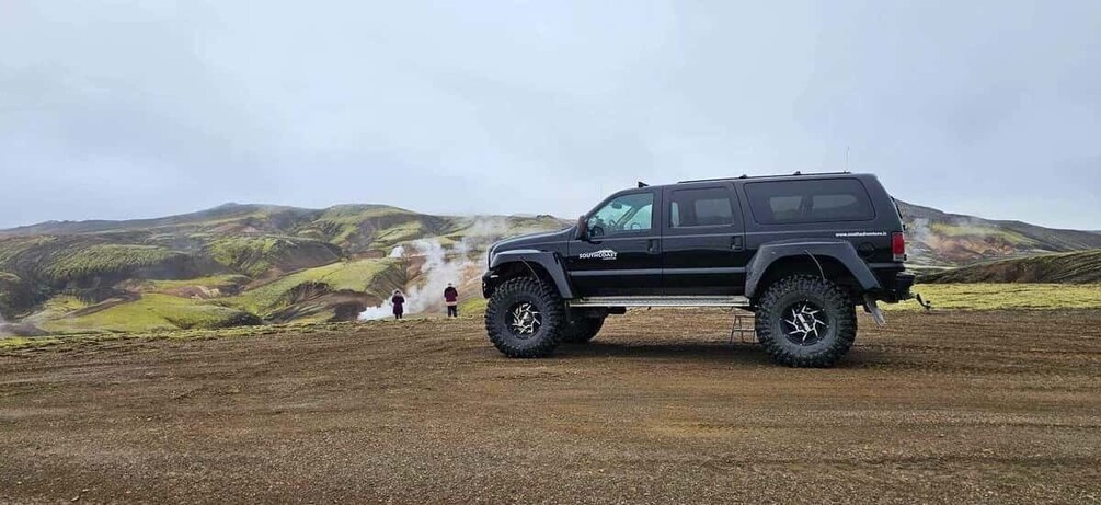 A black SUV parked on a dirt road with a hilly landscape in the background. 2