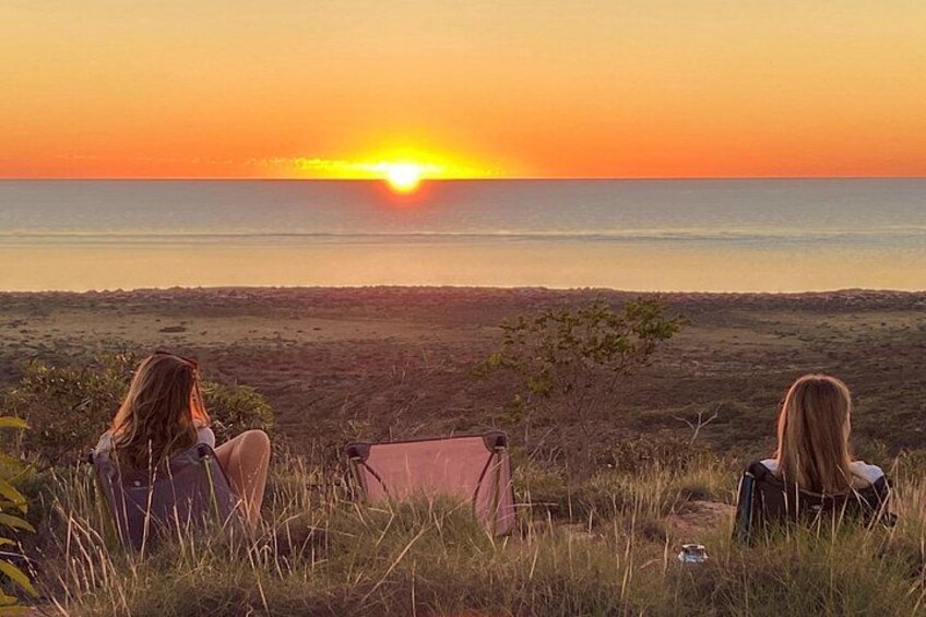A sunset over a beach with three people sitting on chairs. 3