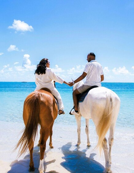 Two people on horseback on a beach with clear blue water and sky. 5