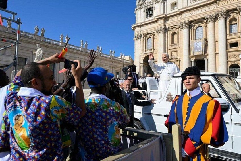 A group of people in colorful attire, a white vehicle, and a building with statues and inscriptions. 2