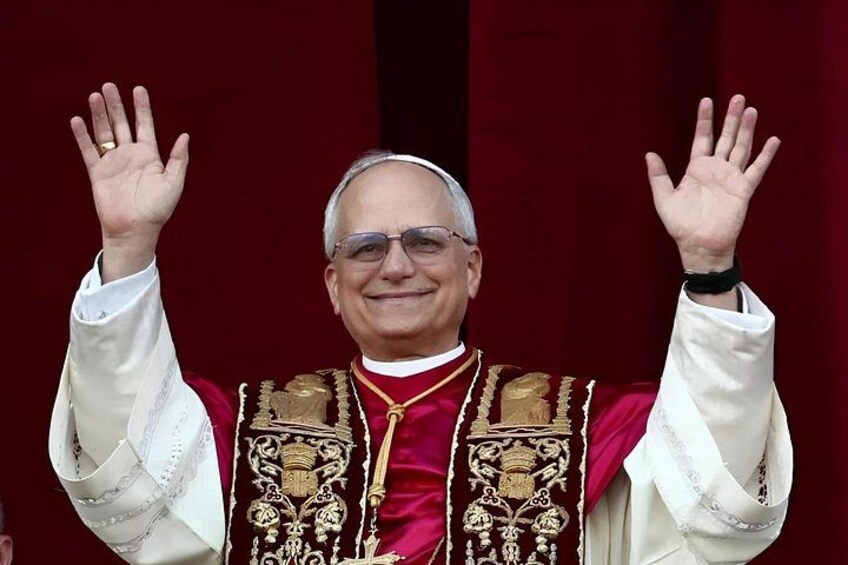 A person in a red and gold ceremonial robe with a white collar and cuffs, raising both hands. 1