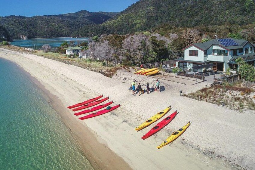 A beach with kayaks lined up, a building, and a forested hill in the background. 2