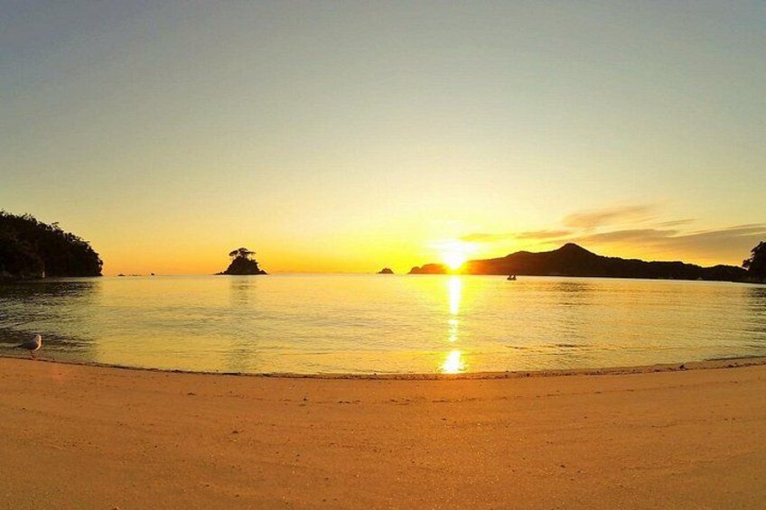 A beach at sunset with calm water, a sandy shore, and distant landforms. 3