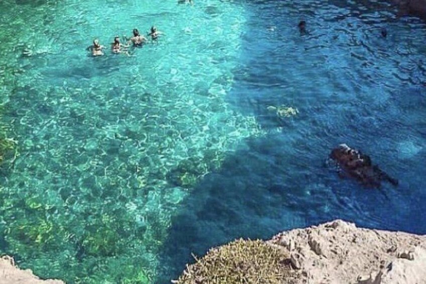 A clear blue water body with people swimming and a rocky shore. 3