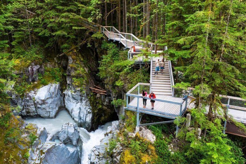 A wooden bridge over a river, surrounded by dense forest and rocky cliffs. 1