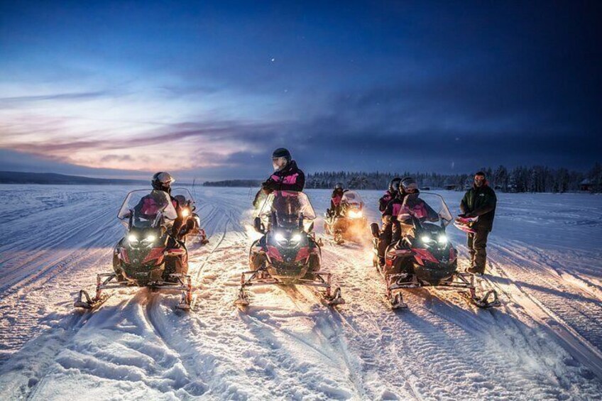 A group of snowmobiles on a snowy field at twilight. 3