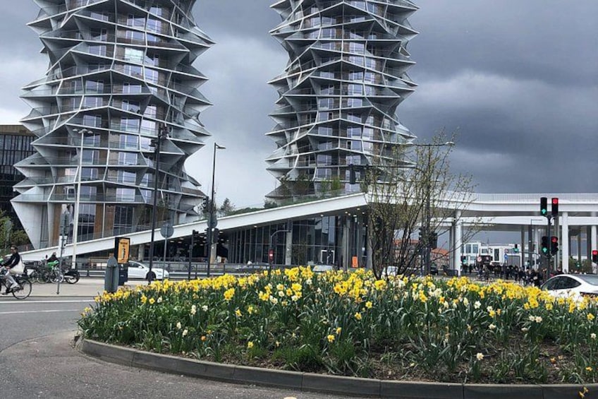 A modern building with a unique spiral design, a flower bed with yellow flowers, and a traffic light. 2