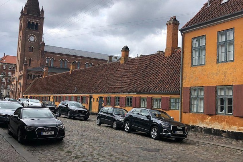 A cobblestone street lined with parked cars and historic buildings with red-tiled roofs. 4