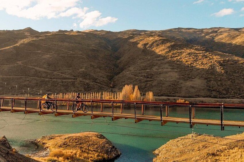 A bridge with cyclists, a river, and a mountainous landscape. 1