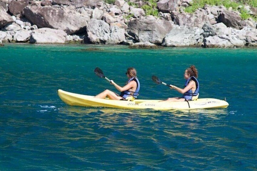 Two people kayaking on a turquoise body of water with a rocky shoreline in the background. 5