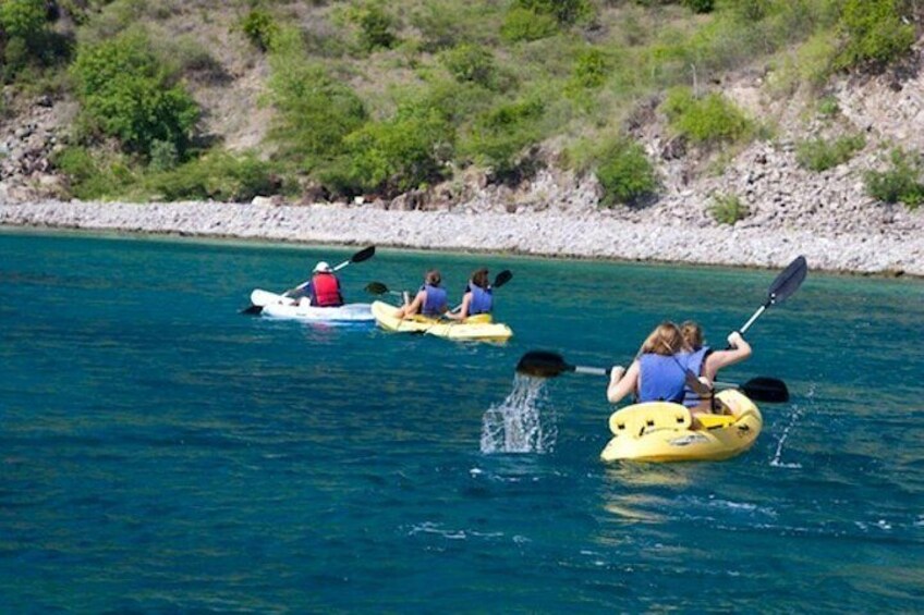 Three kayaks on a calm body of water with a rocky shoreline and greenery in the background. 4