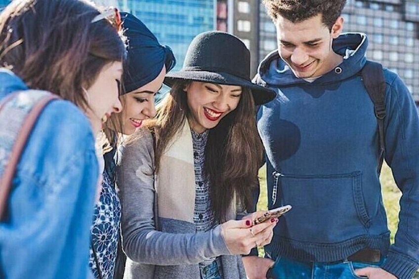 A group of people standing outdoors, looking at a smartphone. 4