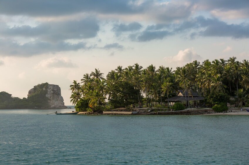 A tropical beach with palm trees, a rock formation, and a thatched-roof hut. 4